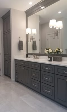 a large bathroom with two sinks and mirrors on the wall, along with gray cabinets