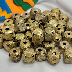 many brass colored beads are laying on a white tablecloth next to a colorful object