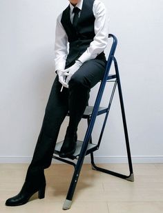 a man sitting on top of a chair wearing a black suit and white dress shirt