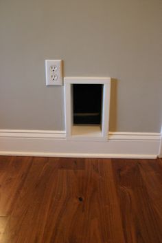 a dog house built into the side of a wall in a room with hardwood floors