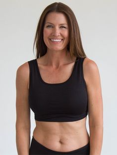 a woman wearing a black sports bra smiling at the camera with her hands in her pockets