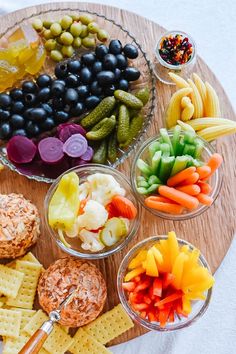 a wooden platter filled with crackers, vegetables and fruit on top of it