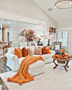 a living room filled with white furniture and lots of orange pillows on top of it