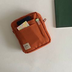 an orange pouch with a notepad and pen sticking out of it next to a green notebook