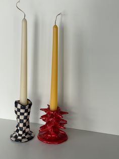 two candles sitting on top of a table next to each other in front of a white wall