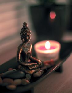 a small buddha statue sitting on top of a table next to a candle and rocks