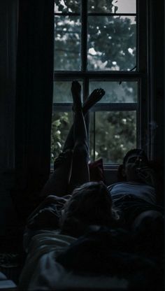 a person laying in bed with their feet up on the window sill looking out