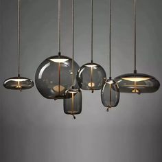 an assortment of glass pendant lights hanging from chains on a gray wall in a room