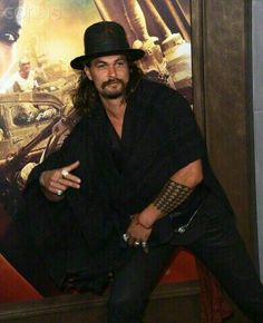 a man with long hair wearing a black hat and holding his finger up in front of a movie poster