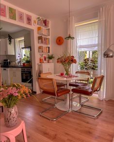 a dining room table and chairs in front of a window with flowers on the windowsill