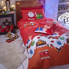 a bed with red sheets and christmas decorations on it, next to a white rug