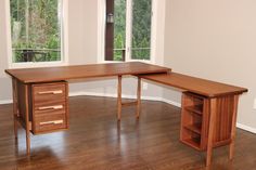 a wooden desk sitting on top of a hard wood floor next to two large windows