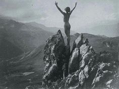 a naked woman standing on top of a rocky mountain with her arms in the air