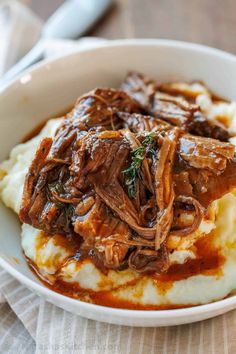 a white bowl filled with mashed potatoes covered in beef and gravy next to a fork