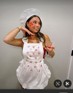 a woman dressed in an apron holding a wine glass and pointing to the side with her finger