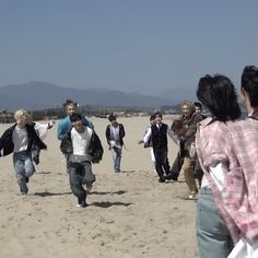 a group of people walking across a sandy beach next to each other on a sunny day