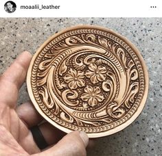 a hand holding a decorative wooden plate on top of a stone floor with the words mosaii leather written below it