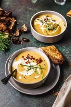 two bowls of soup on a table next to bread and garlic crackers with herbs