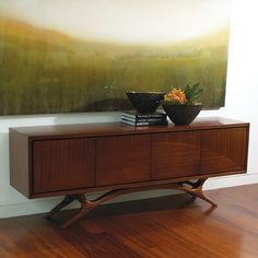 a painting is hanging on the wall above a wooden cabinet with two bowls and books