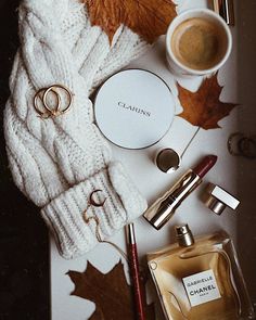 the contents of a white sweater are laid out next to autumn leaves and other items