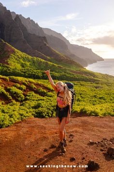 a woman with a backpack is walking up a hill towards the ocean and hills in the background