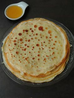 a stack of pancakes sitting on top of a glass plate next to a bowl of syrup