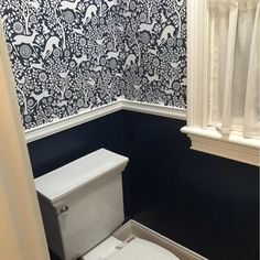 a white toilet sitting in a bathroom next to a wall papered with animal designs