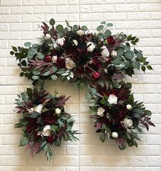 two wreaths with white and red flowers hanging on a brick wall