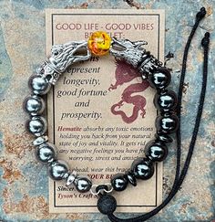 "Introducing the GOOD LIFE/GOOD VIBES bracelet! A bracelet that is beautiful and meaningful.    SYMBOLIC MEANING OF THIS BRACELET: 🔥 Dragon are symbols of prosperity, success and good luck.   The positive energy from this bracelet helps you LIVE YOUR BEST LIFE! This POWERFUL bracelet:   👍 Features silver dragon head beads, with matching hematite spacer beads, 👍 🔥 FIRE DRAGON (red & yellow central bead)  👍 Has 10mm Silver and Grey Hematite Beads, 👍 Is made with durable memory wire so that t Adjustable Hematite Bracelets As Gift, Spiritual Braided Bracelets As A Gift, Spiritual Silver Braided Bracelet Hand-strung, Spiritual Silver Hand-strung Braided Bracelets, Spiritual Round Braided Bracelets As Gifts, Spiritual Braided Bracelet Gift, Spiritual Round Braided Bracelet As Gift, Adjustable Healing Bracelets With Meaningful Style, Spiritual Nickel-free Beaded Bangle Bracelets