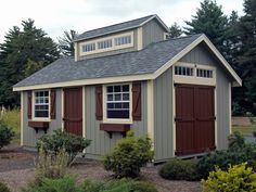 a small shed with two windows and shutters on the roof is surrounded by trees