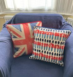 two pillows sitting on top of a blue couch in front of a window with the british flag