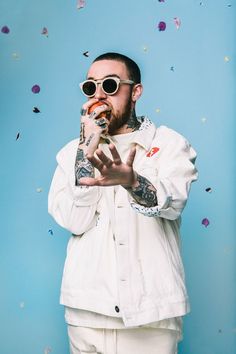 a man with tattoos and sunglasses is holding something in his hand while standing under confetti