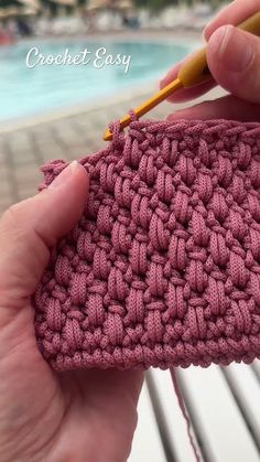 someone is crocheting the stitchs on a pink purse with a yellow knitting needle