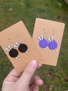 two pairs of purple and black acrylic earrings on top of brown card with grass in background