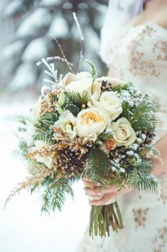 a bridal holding a bouquet of flowers in the snow with pine cones and greenery