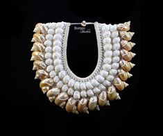 A beautiful handmade white braided Rope curved necklace, decorated with two rows of white curled Shells, and a row spiral golden Mother-of-Pearl Shells. The white curled slices are between, approximately, .8 inch and 1.1 inches in drop length and the Mother Of Pearl Shells are between, approximately, 2 inches and 2.25 inches in length. The inner diameter of the necklace is 4 inches, and the outer diameter is 13 inches. The necklace has a drop length of 12 inches, and is attached, at the top, by White Unique Shell Necklace, White Handwoven Necklace For Festivals, White Handwoven Festival Necklace, Unique Handmade White Shell Necklace, Unique White Handwoven Jewelry, Unique Handwoven White Jewelry, Handmade White Shell Necklace, Unique White Beaded Necklaces For Beach, Festival White Shell Necklace