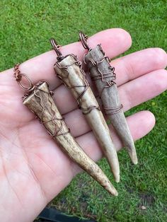 three different types of animal tooth pendants on a person's hand in the grass