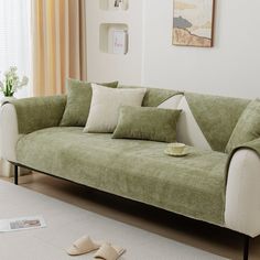 a living room with a green couch and pillows on the floor next to a window