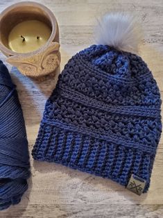 a blue knitted beanie next to a cup of coffee and yarn on a wooden table