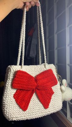 a crocheted purse with a red bow on the front and white bottom, held by a woman's hand