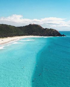 people are swimming in the clear blue water near an island with white sand and green trees