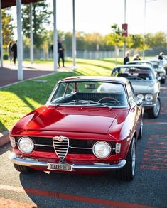 an old red car is parked on the side of the road in front of other cars