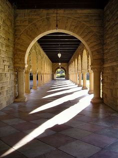 an arched walkway between two buildings with stone pillars and arches on both sides, leading into the distance