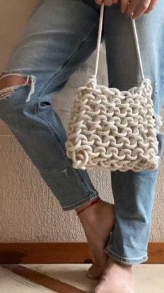 a woman is holding a white purse with chains on the handles and bottom, while wearing ripped jeans