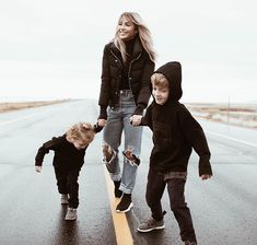 a woman and two children are walking down the street on a skateboard with their hands in each other's pockets