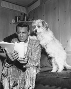 a man sitting on a couch next to a dog and holding something in his hand