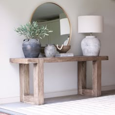 two vases are sitting on a wooden table with a mirror in the corner behind it