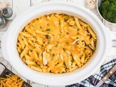 a white bowl filled with pasta and cheese on top of a wooden table next to utensils