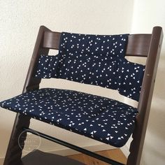 a wooden rocking chair with blue and white fabric on it's seat cushion, in front of a wall