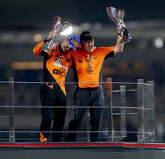 two men holding up trophies on top of a race track